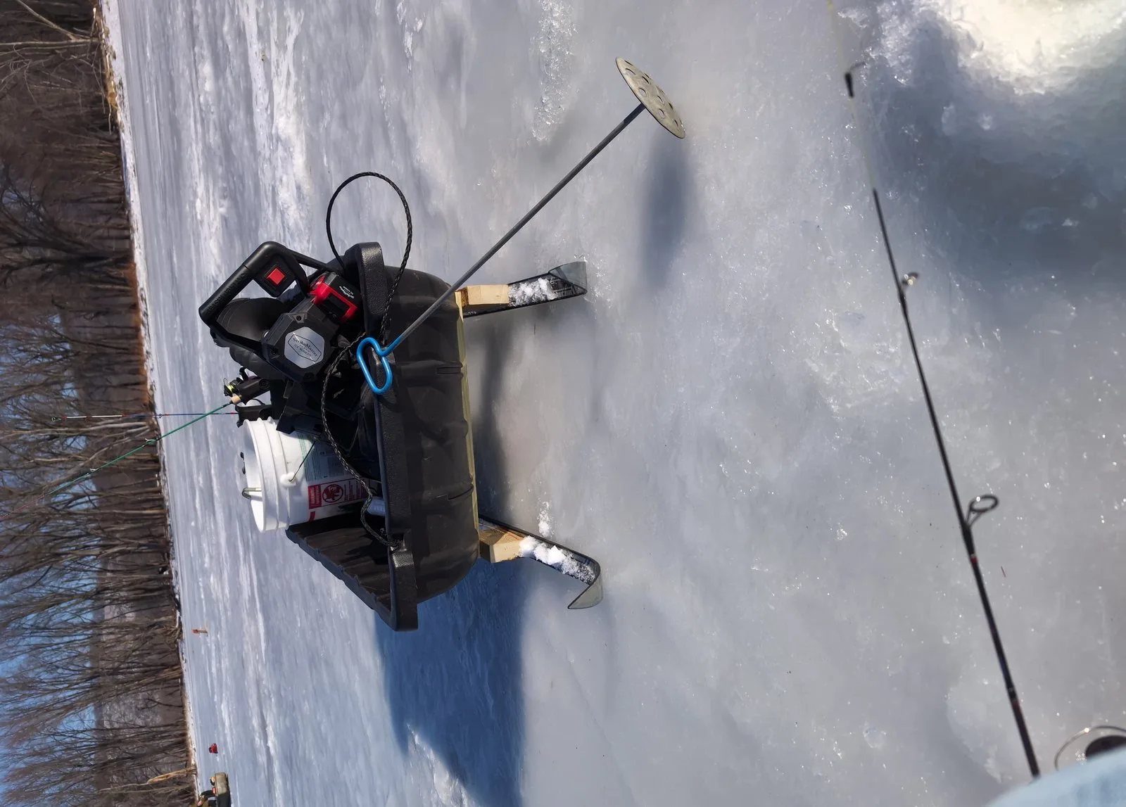 Ice fishing sled, sonar, auger, and rod arranged on the ice
