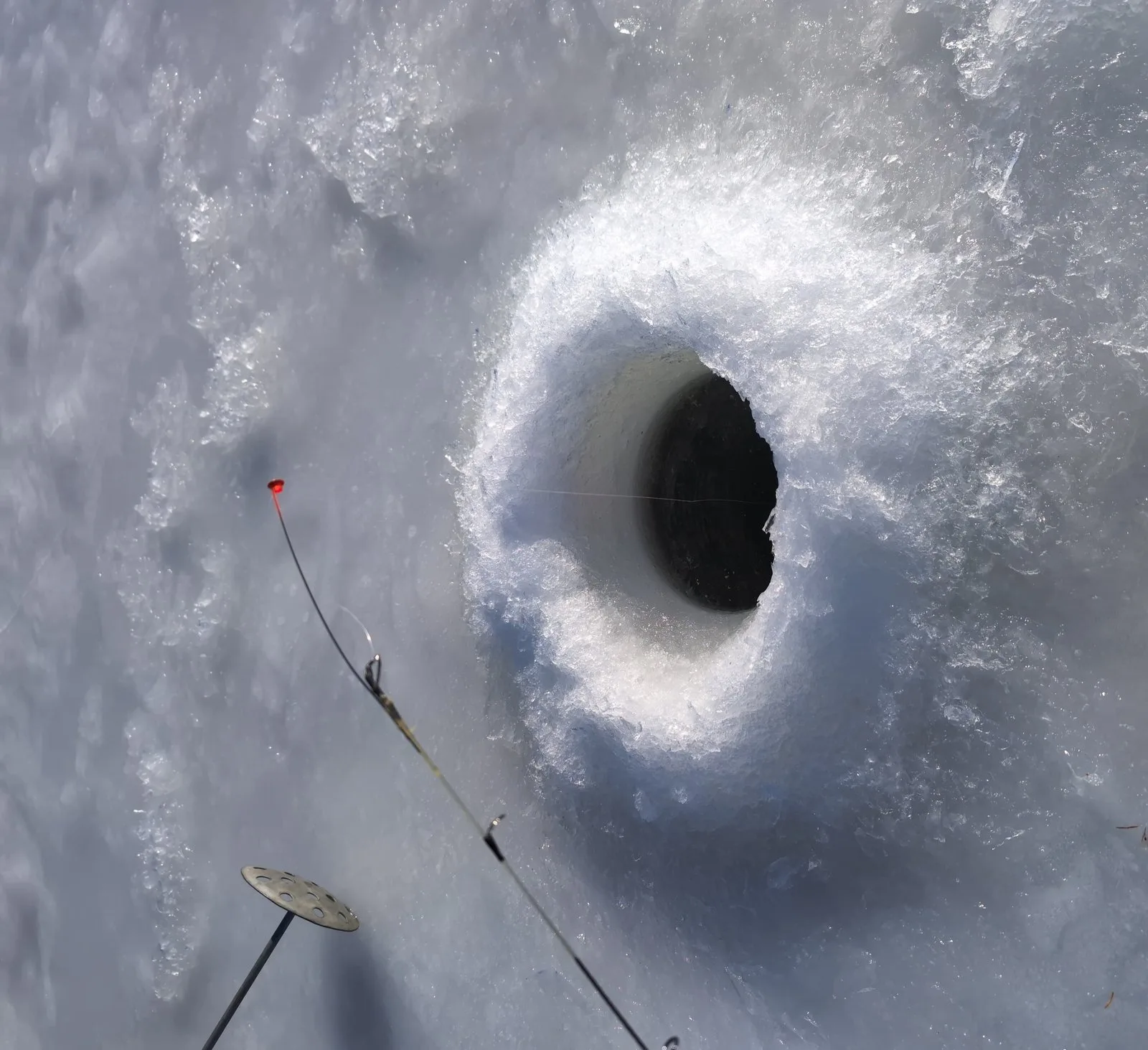 Top-down view of an ice fishing hole with tip-up gear